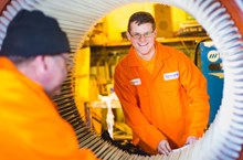 A young man wears an orange jumpsuit while working at his engineering apprenticeship.
