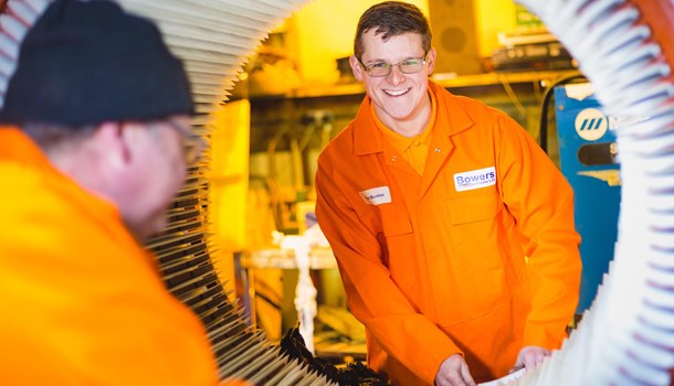 A young man wears an orange jumpsuit while working at his engineering apprenticeship.
