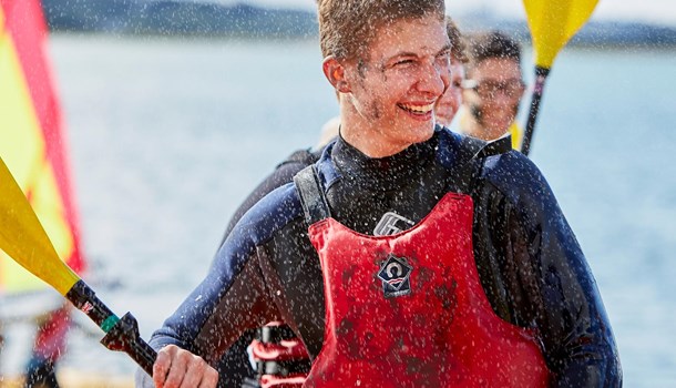 Three deaf young men smile while paddling a kayak.