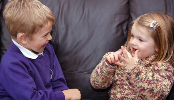 A young girl signing to a young deaf boy on a sofa