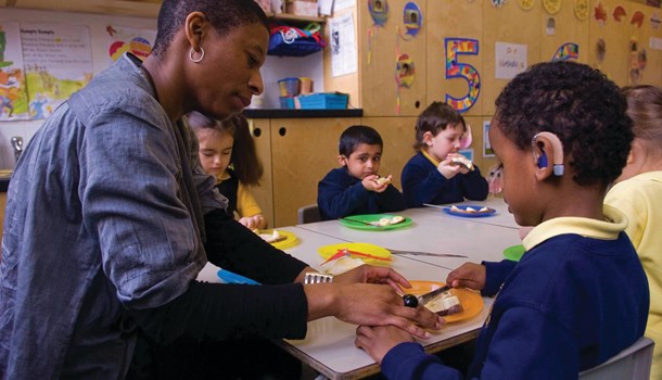 A primary teacher helps a young boy wearing hearing aids with his lunch.