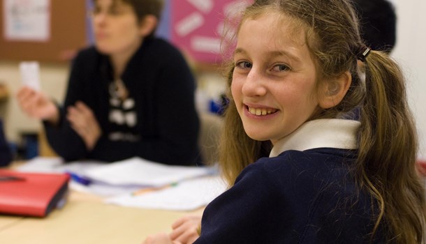 A girl in a classroom turns around to smile at the camera. 