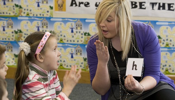 A teacher practices phonics with a girl wearing a hearing aid.