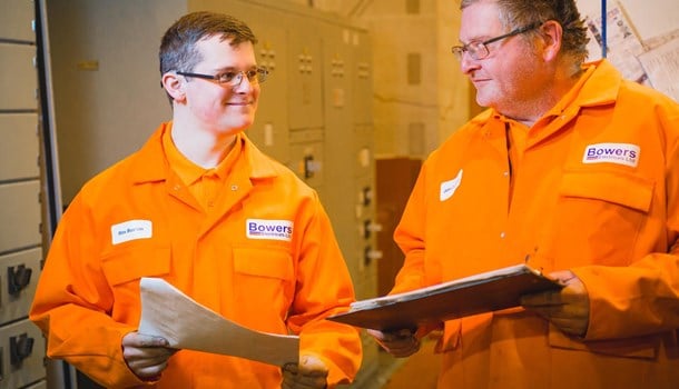 A young deaf man in an orange jumpsuit with a colleague at his engineering apprenticeship.