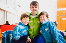 Three children in walking jackets hugging in a group looking directly at the camera.