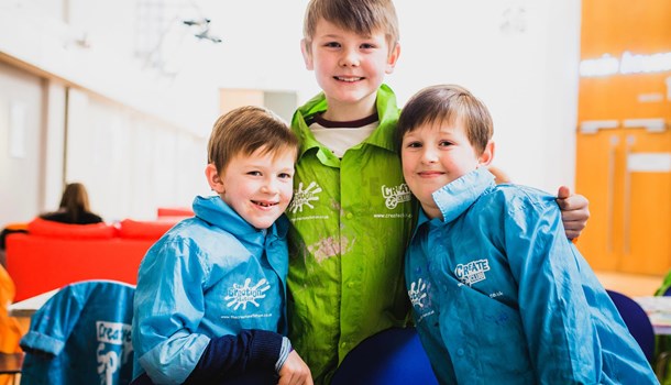 Three children in walking jackets hugging in a group looking directly at the camera.
