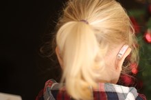 Child with blonde hair facing away from the camera, their hearing aid can be seen on their right ear.