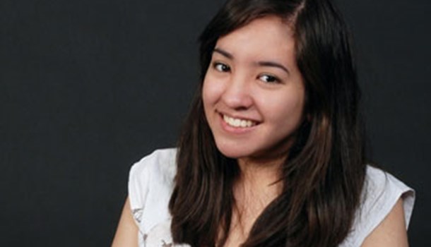 A professional headshot of a deaf young woman wearing white against a black background.