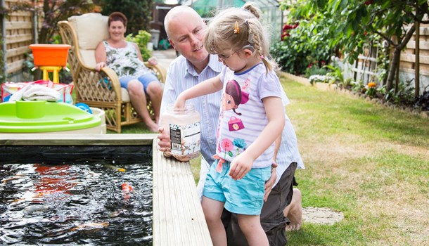Leia and her dad feeding fish in a pond in their garden with mum lounging in the background.