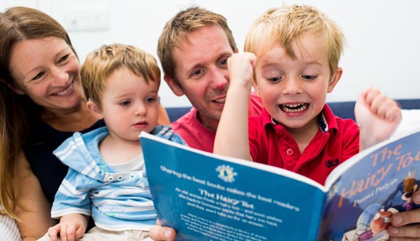 Charlie excitedly reading a book sat with his parents and younger brother.