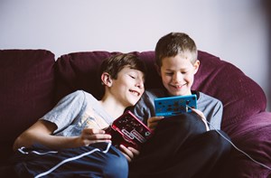 Two brothers play their Nintendos next to each other on the sofa. 