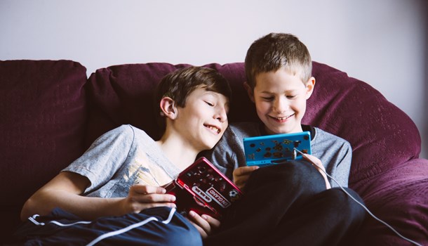 Two brothers play their Nintendos next to each other on the sofa. 