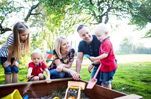 A family with three children play in a sandbox outside.