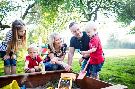 A family with three children play in a sandbox outside.
