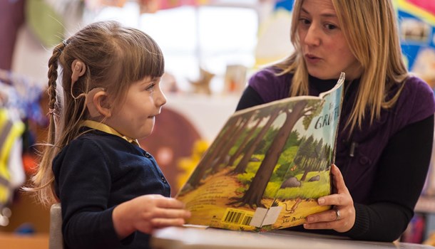 A teacher reads The Gruffalo with a girl wearing a cochlear implant.