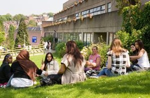 A group of students sit in a study circle on the lawn by a campus building.