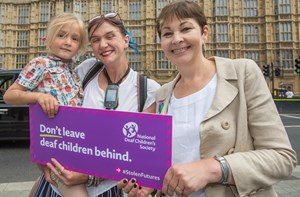 MP Caroline Lucas with mother Kelly and her deaf son Thomas, holding a sign that reads, 'Don't leave deaf children behind.'