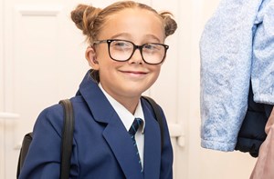 A girl wearing her school uniform and backpack smiles at the camera. 