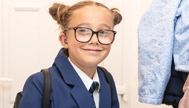 A girl wearing her school uniform and backpack smiles at the camera.