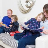 Jemima reading with her mum and her sister reading with their dad on the sofa.