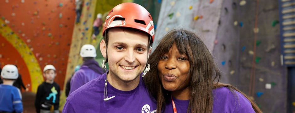 Two volunteers smiling in front of a climbing wall.