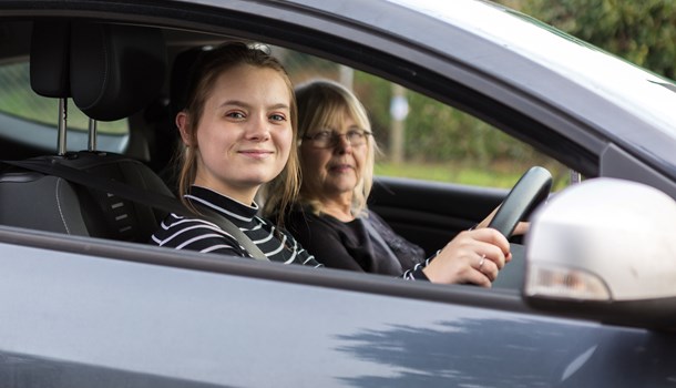 A teenager smiles confidently from the driver's seat of a car.