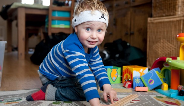 A toddler wearing a bone conduction soft headband plays with toys on the floor. 