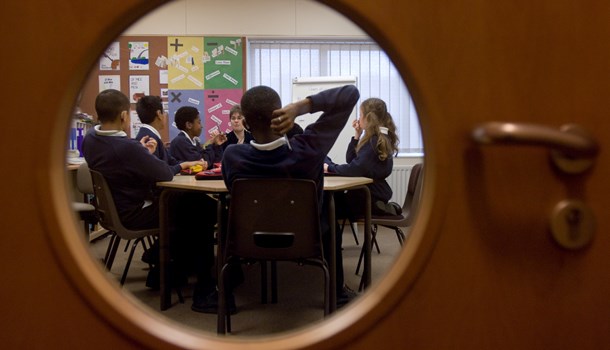 A photo taken through a round window of a group of students sitting around a table in their classroom.