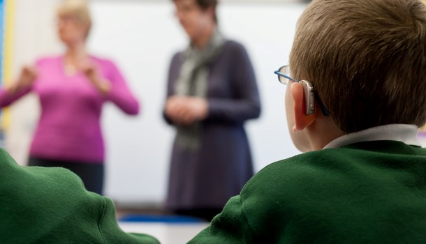 The back of a boy's head who is wearing hearing aids and sitting in a classroom.