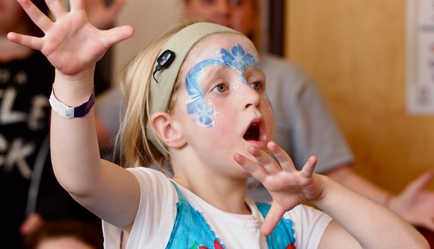 A girl with a hearing headband wears face paint and motions with her arms