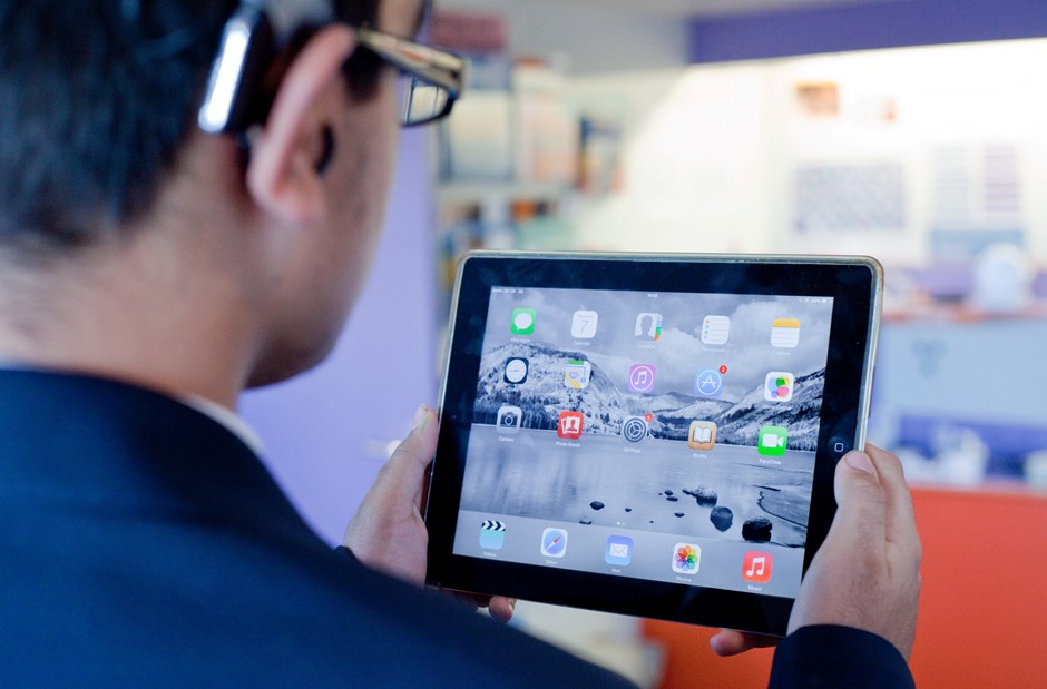 A young man wearing a hearing aid looks at a tablet device