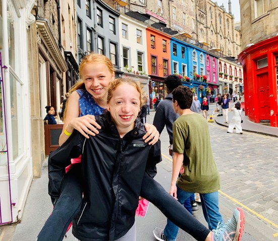 Girl giving her younger sister a piggy back outside on a colourful street