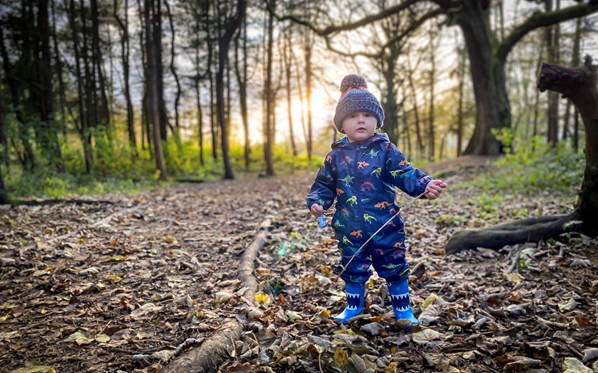 Little boy in dinosaur print onesie in the woods
