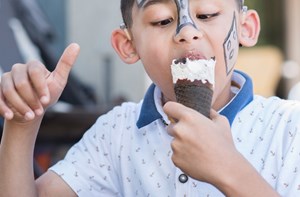 A boy wearing face paint happily eats an ice cream cone. 