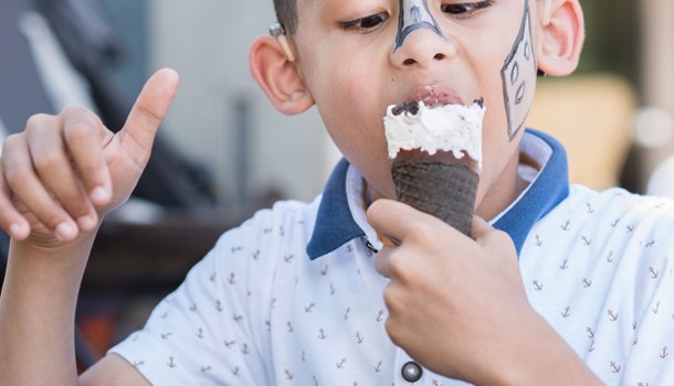 A boy wearing face paint happily eats an ice cream cone. 