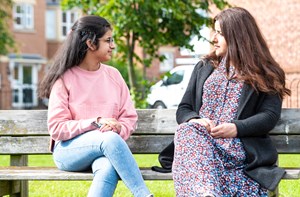 A teenager talks to her mum on a park bench.