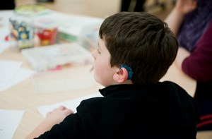 The back head of a boy wearing a hearing aid sitting at a table with other children. 