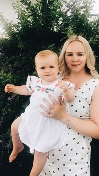 Mum holding her baby daughter, both wearing white patterned dresses