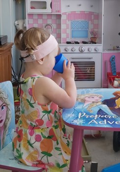 Little girl with cochlear implants wearing a printed dress sitting at a table