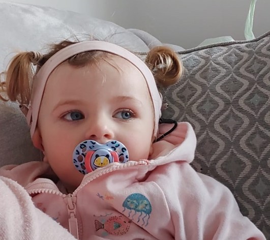 Little girl with cochlear implants sitting on the sofa using a dummy