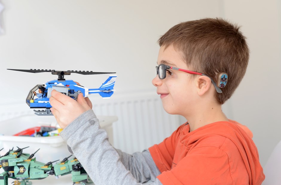A boy with a bone conduction hearing device abutment plays with a toy helicopter