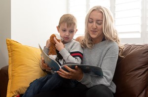 A woman and young boy reading a book on the sofa