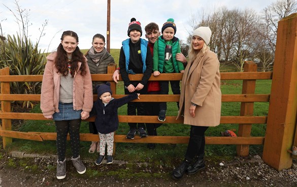 Seven children between the ages of 2 and 19 standing against a wooden fence outside