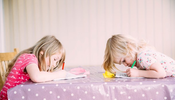 Two young sisters draw in colouring books at their table. 