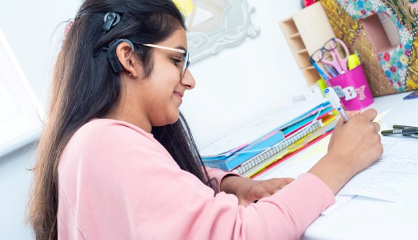 A deaf teenager wearing a cochlear implant works on homework at her desk.
