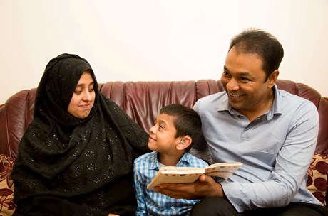 A mum and dad read a book to their boy, while the boy smiles up at his mum.