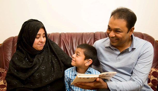 A mum and dad read a book to their boy, while the boy smiles up at his mum.