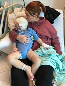 Little boy lying on his mum after cochlear implant surgery