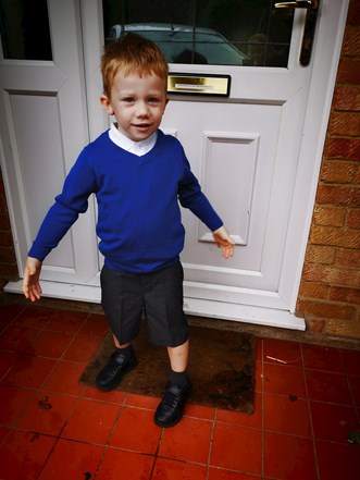Little boy standing outside the front door to a house wearing primary school uniform