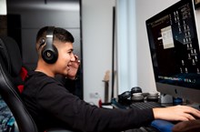 A teenager works at a desktop computer with headphones over his ears.
